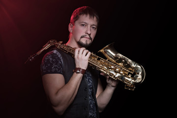 Naklejka premium Serious bearded saxophonist with sax on the shoulder isolated against a black background