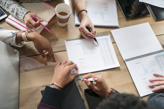 Cropped image of colleagues discussing graphs at table in office