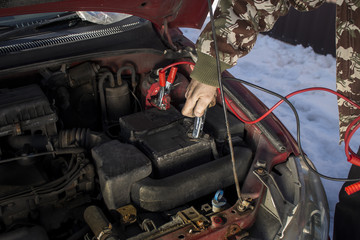 Mechanik podłącza kable rozruchowe do rozładowanego akumulatora. Odpalanie samochodu zimą przez...