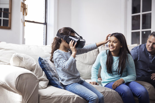 Father and daughter looking at girl wearing virtual reality simulator while sitting at home
