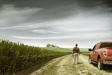 Rear view of farmer standing by car on field against cloudy sky