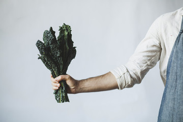 Midsection of man holding kale while standing against white wall at home