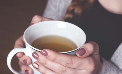 Junge Frau wärmt Hände an Teetasse.