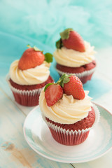 Three pink white cupcakes with strawberries on a blue wooden table. Selective focus