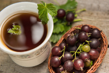 Berry black currant in a basket on a wooden background with Cup of tea