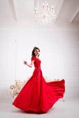 Elegant woman in a long red dress is standing in a white room chic, swirl dress
