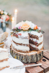 Beautiful sliced wedding cake decorated with flowers on wooden circle outdoor