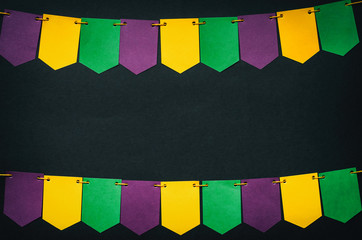 Handmade paper flags garland border, black background. Mardi Gras vibrant colorful postcard,...