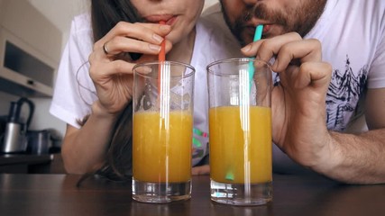 Young woman and man drinking orange juice with straws. Healthy lifestyle or funny competition concepts. 4K clip - Powered by Adobe