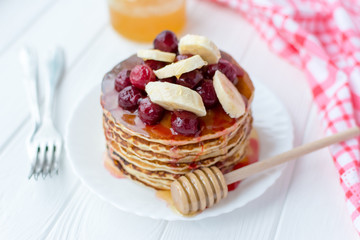 Healthy breakfast. Stack of delicious, homemade pancakes with honey, cherry and banana on white plate 