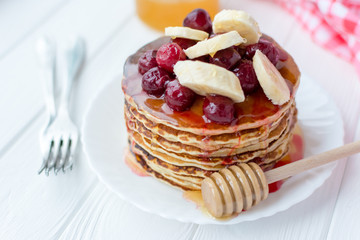 Healthy breakfast. Stack of delicious, homemade pancakes with honey, cherry and banana on white plate 