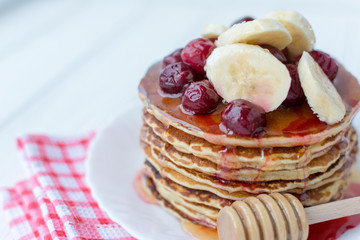 Healthy breakfast. Stack of delicious, homemade pancakes with honey, cherry and banana on white plate 