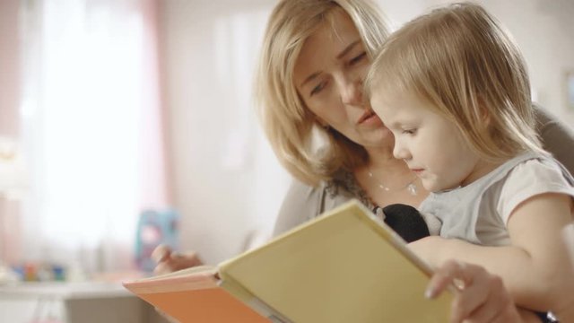 Cute Little Girl Sits on Her Grandmother's Lap and They Read Children's Book. Slow Motion. Shot on RED EPIC-W 8K Helium Cinema Camera.