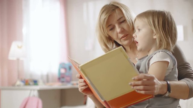 Cute Little Girl Sits on Her Grandmother's Lap and They Read Children's Book. Slow Motion.  Slow Motion. Shot on RED EPIC-W 8K Helium Cinema Camera.