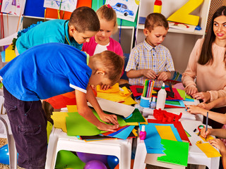 Children cutting paper in class. Kids development and social lerning children in school. Children's project in kindergarten. Low tables for work and creativity. Group girl , boy with teacher together.