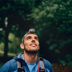 Fit male jogger with a headlamp rests during training for cross country trail race in nature park. © AYAimages