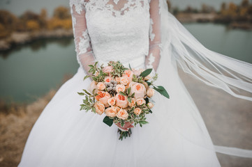 Wedding bouquet of pink roses in bride's hands on a background of lake