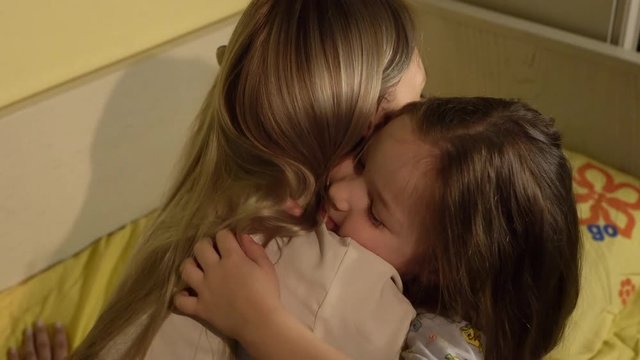 Mother hugging her daughter goodnight in bedroom.