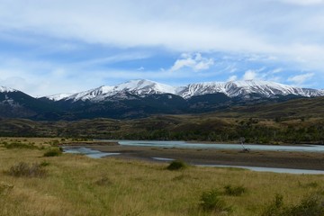 Naklejka na ściany i meble Fresh snow melt stream flowing through a beautiful open meadow surrounded by snow capped mountains in Torres del Paine National Park. 