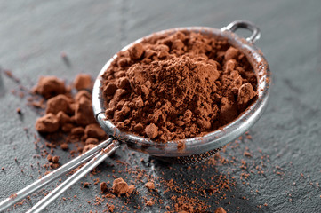 sieve with cocoa powder close-up on black slate plate 

