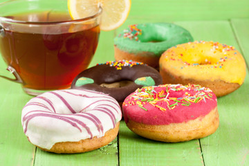 pile of glazed donuts with a cup of tea on a green wooden background