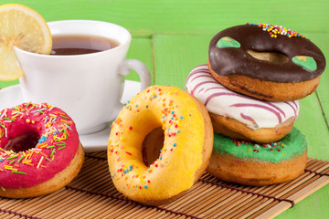 pile of glazed donuts with a cup of tea on a green wooden background