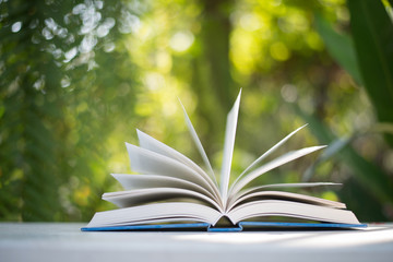 Close up of open book at home garden with nature bokeh background.