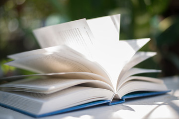 Close up of open book at home garden with nature bokeh background.