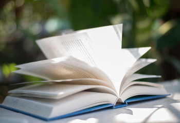 Close up of open book at home garden with nature bokeh background.