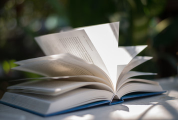 Close up of open book at home garden with nature bokeh background.