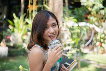 Happy beautiful student girl holding folders and books walking drinking iced drink outdoors at home garden.