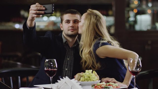 man taking selfie with woman and they kissing each other in cheeks