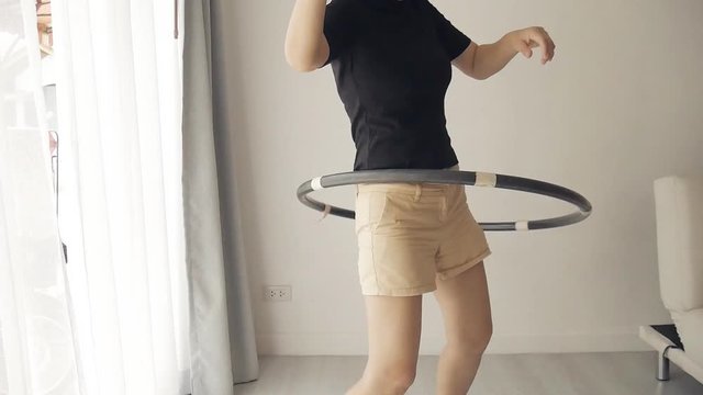 Woman is doing a Hula-Hoop workout in a living room at her house