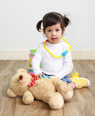 Little asian girl or a little cute asian girl doctor examining teddy bear