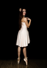 Young ballerina with a perfect body is dancing in pointe shoes on dark background