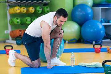 Male athlete kneeling down by dumbbells toweling sweat of his brow.