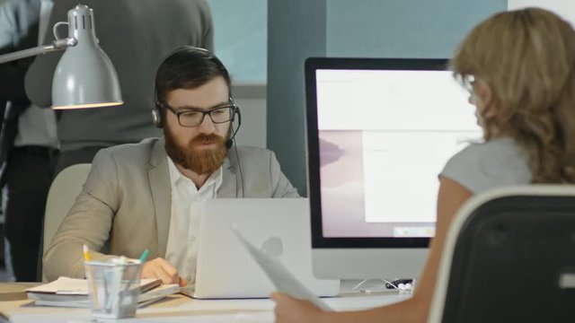PAN of bearded businessman in headphones talking with partners on video call in busy office 