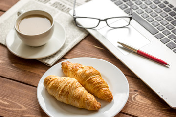 Business lunch with croissant and laptop on wooden desk