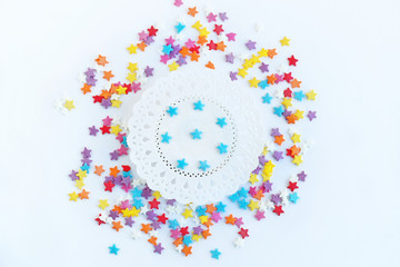 colorful confectionery sprinkling of sweet stars confetti and white lacy paper doily on abstract light background