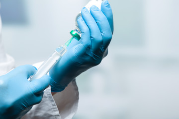 Hand mit Handschuhen zieht eine Spritze auf