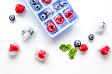Ice tray with berries and mint on white background top view
