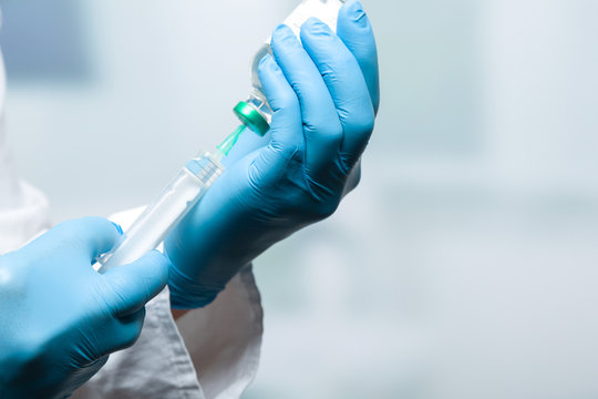 Hand mit Handschuhen zieht eine Spritze auf