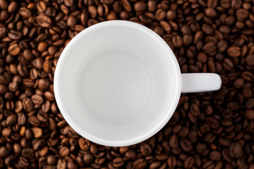 Empty white mug among coffee beans, top view