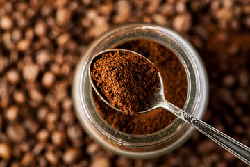 Ground coffee in a metal spoon on a top of glass jar, shallow depth of field