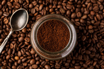Metal spoon with coffee beans and ground coffee in a glass jar