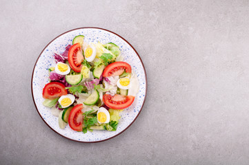 Fototapeta na wymiar Fresh salad with vegetables tomatoes, cucumbers, lettuce, salad leaves and eggs on grey background top view and copy space. Healthy food and diet concept. Vegetarian food