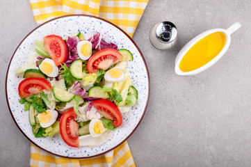 Fresh salad with vegetables tomatoes, cucumbers, mix salad leaves, eggs and olive oil on grey background top view. Healthy food and diet concept. Vegetarian food