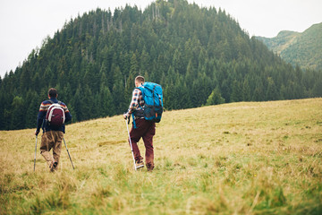 Fototapeta na wymiar Hikers walking in a field towards forested hills