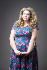 Young beautiful happy blonde plus size model in dres, xxl woman portrait on gray studio background