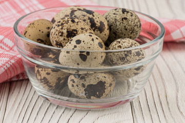 Quail eggs in a glass bowl on old white wooden table.